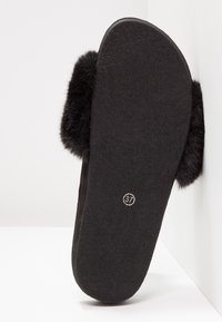 Pantoufle noire avec des accents en fourrure douce, semelle plate et matériau texturé. Taille 37 indiquée au fond. Forme simple et arrondie.