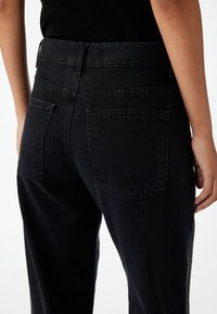 Jeans de mezclilla negra con cintura alta, que presentan dos bolsillos traseros, un diseño de pierna recta y un detalle de panel lateral texturizado.