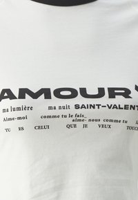 Witte katoenen t-shirt met zwarte bedrukt tekst met zinnen, waaronder "AMOURY" en "SAINT-VALENTIN," met een klassieke ronde halslijn.