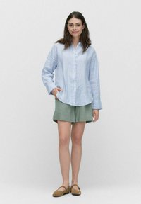 Ljusblå och vit randig skjorta med knappar och långa ärmar, matchad med lösa gröna shorts. Tyget ser mjukt ochAndandande ut.