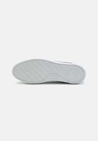 Semelle de sneaker blanche avec un motif texturé, présentant un bord arrondi et un détail de logo sur le côté. Matériau en caoutchouc lisse, design minimaliste.