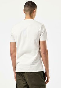 T-shirt med korte ærmer og rund hals i lys beige bomuld. Glat tekstur, ingen synlige mønstre, med et ensfarvet design på ryggen.