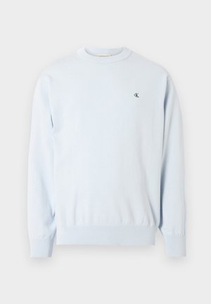 Lys blå langermet genser med rund hals, ribbestrikkede mansjetter og nederkant, med en liten svart "CK"-logo på venstre bryst.