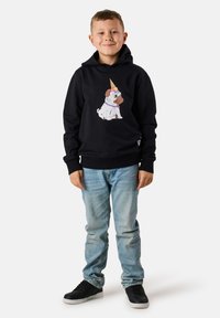 Felpa nera con cappuccio che presenta un cane in stile cartone animato che indossa un colorato cappello a forma di cono gelato, abbinata a jeans azzurri chiari e scarpe da ginnastica nere.