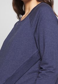 Camiseta de manga larga azul marino con cuello redondo y mangas raglán; confeccionada en un suave tejido texturizado con un acento de canalé a lo largo del lateral.