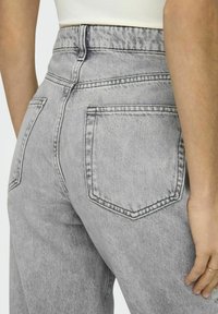 Jean de tiro alto en denim gris claro con un acabado desgastado, que cuenta con dos bolsillos traseros y costuras en contraste. Textura suave.