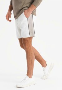Herre shorts i hvid med grå panel og sort kant. Parret med hvide sneakers. Stoffet ser blødt ud, afslappet pasform.