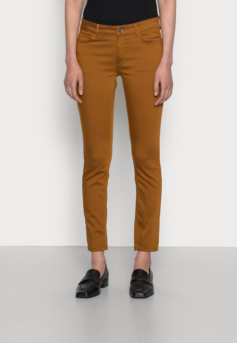 Pantalon en coton marron ajusté avec quatre poches, une fermeture par bouton à l'avant et un design sans couture. Associé à des mocassins noirs pour le contraste.