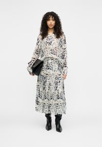 Μπλούζα με μακριά μανίκια και αντίστοιχη φούστα από ελαφρύ ύφασμα με αφηρημένα μπλε και μαύρα σχέδια. Συνδυάζεται με μαύρες μπότες μέχρι το γόνατο και μαύρη τσάντα.