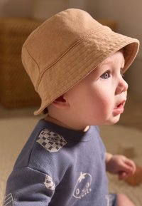 Chapeau bob en coton beige avec une texture douce, associé à un t-shirt bleu à col rond orné de motifs blancs ludiques sur les épaules.