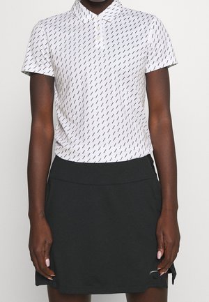 Personne portant un polo blanc à manches courtes avec des lignes diagonales noires et une jupe noire avec un petit logo près de l'ourlet.