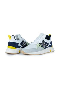 Zapatillas para hombre con una mezcla de malla blanca y ante azul marino, detalles en verde lima, logo negro y una suela de goma con una lengüeta en el talón de color amarillo.