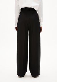 Zwarte wijde broek van gladde stof, met een hoge taille, geplooide voorkant en een enkele achterzak, gecombineerd met een wit shirt.