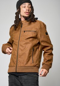 Veste en simili cuir marron avec fermeture éclair sur le devant, poignets côtelés et finition texturée. Comprend une poche zippée et des accents de design perforés.