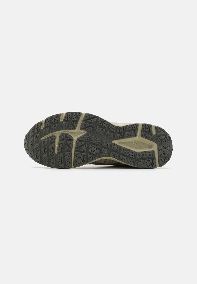 Suela de zapato con una suela exterior de goma texturizada de color gris oscuro, que presenta un patrón geométrico y acentos beiges a lo largo del borde para aumentar la tracción.