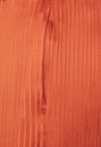 Tecido com a cor ferrugem, texturizado, com riscas verticais e um pequeno bolso. O material parece macio e ligeiramente brilhante.