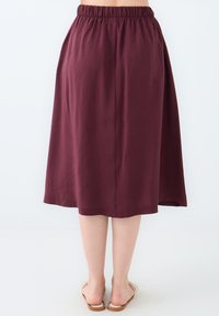 Jupe bordeaux, longueur genoux avec une taille élastique, fabriquée dans un tissu doux, présentant une texture lisse et un design simple et fluide.