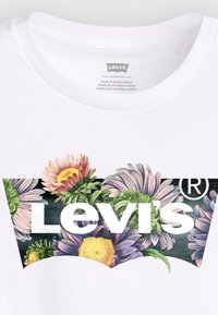 T-shirt blanc avec un graphique floral coloré comportant des fleurs violettes, roses et jaunes ; logo Levi's en texte blanc gras.