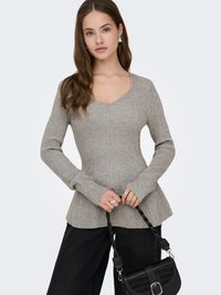 Pull gris côtelé à manches longues avec col en V et ourlet évasé. Le mannequin tient un sac à main noir texturé avec un détail boucle.