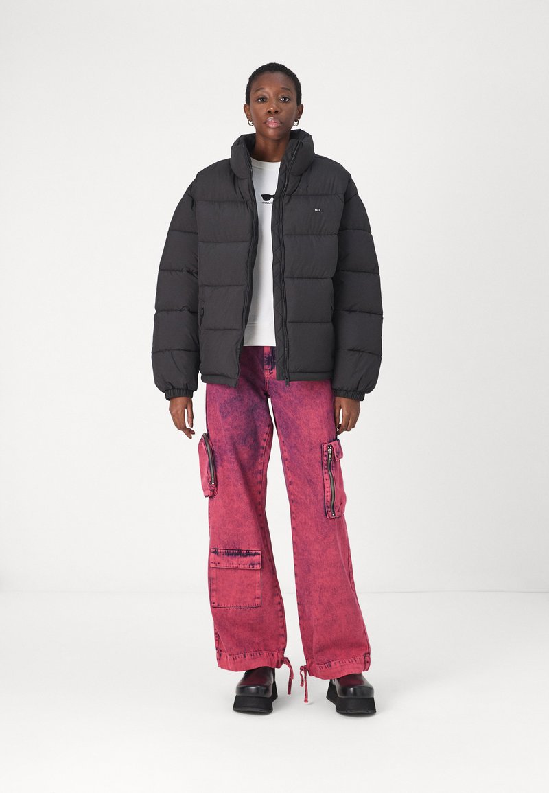 Giacca puffer nera con colletto alto, abbinata a pantaloni cargo rosa larghi con tasche cargo. Stivali neri spessi completano il look.