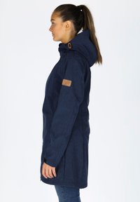 Navy blue hooded jacket with a textured finish, featuring a leather patch on the sleeve and a straight cut; includes pockets and adjustable hood.