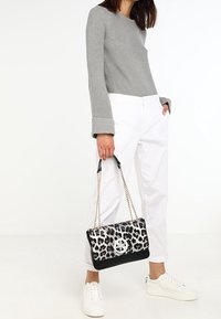 Černobílá kabelka s leopardím potiskem a řetízkovým popruhem, texturovaným povrchem a kulatým logem jako ozdobou. Kombinována se šedým svetrem a bílými kalhotami.