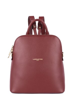 Sac à dos en cuir bordeaux avec une texture lisse, des accents en matériel doré, deux poignées supérieures et des bretelles réglables. Présente un logo.