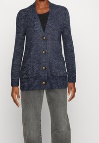 Cardigan a maglia navy con collo a scialle, chiusura con bottoni, due tasche frontali e polsini a coste; presenta una texture di filato screziato.
