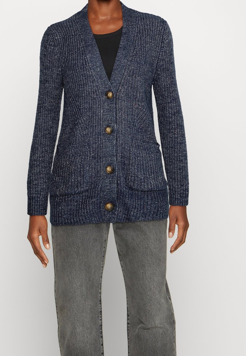 Cardigan a maglia navy con collo a scialle, chiusura con bottoni, due tasche frontali e polsini a coste; presenta una texture di filato screziato.