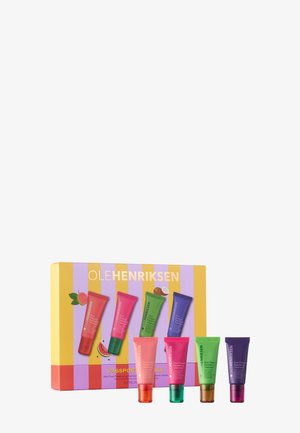 Vier bunte Lippenpflege-Tuben von Ole Henriksen vor einer gestreiften lila-gelben Box mit Fruchtabbildungen.