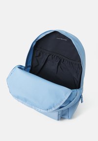 Sac à dos bleu clair en tissu lisse. Il dispose d'une fermeture éclair, d'une doublure intérieure noire et d'une poche avant pour un rangement supplémentaire.