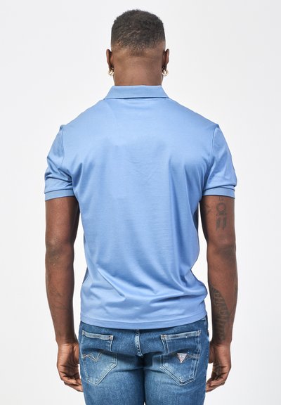Polo shirt azzurro chiaro con maniche corte, texture liscia e colletto classico; abbinato a jeans in denim aderenti con dettagli nelle tasche posteriori.