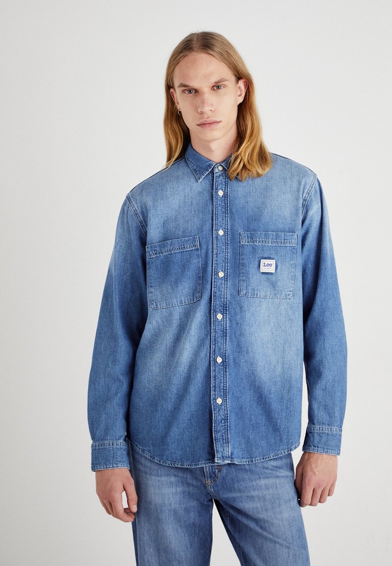 Jasnoniebieska koszula dżinsowa z długimi rękawami, dwiema kieszeniami na piersi i kołnierzykiem zapinanym na guziki. Posiada małą metkę na lewej kieszeni.