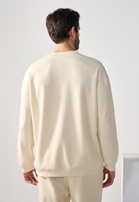 Crewneck sweatshirt i lyse beige, laget av et teksturert stoff. Har droppede skuldre og ribbede mansjetter, med en avslappet passform.