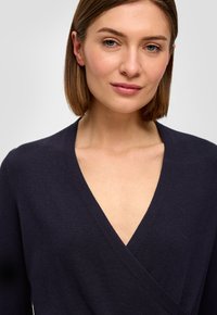Granatowy sweter zapinany w talii, wykonany z miękkiej dzianiny, z głębokim dekoltem w kształcie V i długimi rękawami, o gładkiej fakturze.