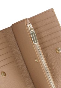 Interno di un portafoglio in pelle marrone chiaro con chiusura a zip, multiple fessure per carte e dettagli in metallo dorato. Dettaglio della superficie testurizzata visibile.