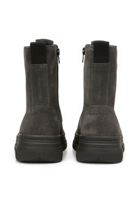 Bottines en daim gris avec une semelle en caoutchouc noir, dotées d'une fermeture éclair et d'une languette tressée pour un enfilage facile. Texture lisse et design minimaliste.