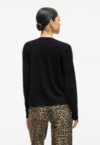 Μαύρος πλεκτός σκούφος με στρογγυλή λαιμόκοψη και ραμμένο τελείωμα, συνδυασμένος με παντελόνι σε λεοπάρ σχέδιο. Η υφή φαίνεται απαλή και άνετη.