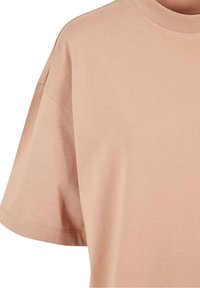 T-shirt beige à manches courtes avec un col rond et des coutures visibles aux ourlets des manches et aux coutures des épaules.