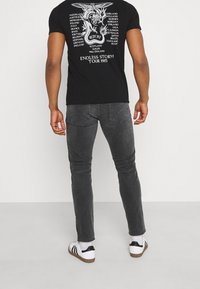 Camiseta gráfica negra con un diseño de dragón blanco en la espalda. Combinada con jeans ajustados grises y zapatillas blancas con detalles negros.