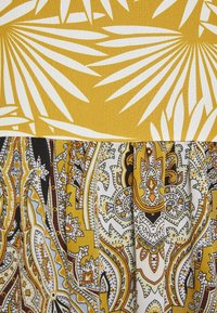 Tela con estampado floral en amarillo y blanco en la parte superior que se transforma en un diseño de cachemira en amarillo, negro y crema en la parte inferior.