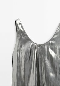 Robe métallisée argentée sans manches avec un tissu brillant et réfléchissant et un décolleté arrondi sur fond blanc.