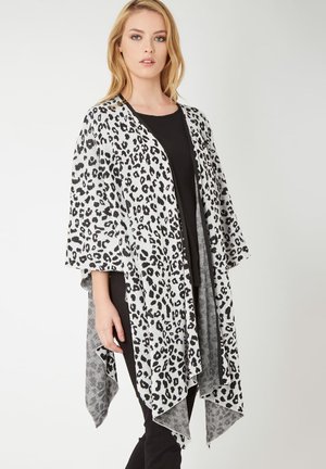 Mujer con un conjunto negro y un chal abierto con estampado de leopardo blanco y negro, con mangas anchas y dobladillo asimétrico.
