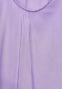 Tissu violet avec une texture lisse, présentant un col rond et un drapé subtil. Le matériau semble léger et fluide.