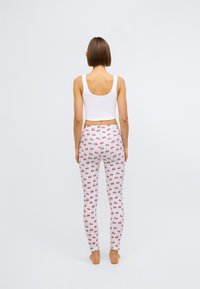 Débardeur blanc court associé à des leggings ajustés présentant un motif de cerises rouges sur fond blanc. Texture de tissu lisse.