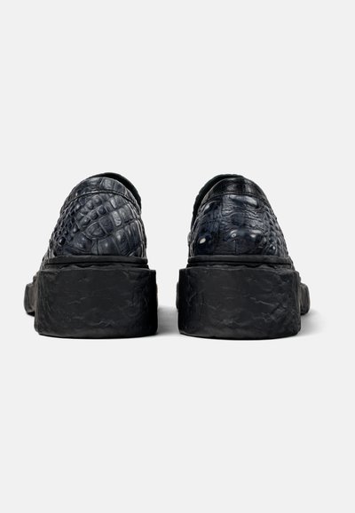 Black slip-on shoes with a textured, crocodile-like pattern and chunky black soles. The back view shows a smooth upper with no visible hardware.