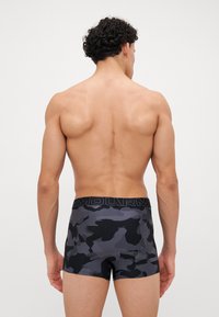 Calzoncillos tipo boxer con patrón de camuflaje en negro y gris, con una cintura elástica negra sólida que presenta "ARMOUR" en letras negritas y contrastantes.
