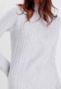 Pull tricoté gris clair avec une texture côtelée et des motifs torsadés, un col montant et des manches longues. Matière douce et confortable.