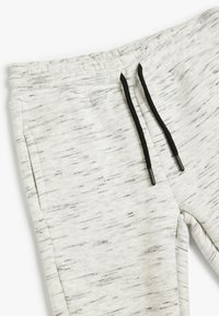 Pantalones de chándal gris claro con un sutil patrón texturizado, que cuentan con un cordón negro y bolsillos laterales. Tejido suave y elástico.