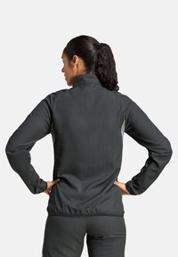 Schwarze Sportjacke mit hohem Kragen, langen Ärmeln und figurnahem Design. Sie verfügt über eine dezente Struktur und einen elastischen Saum am Bund.